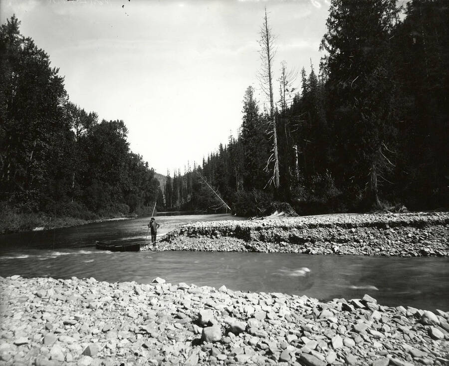 Canoes and a man on the bank at the mouth of Prichard Creek, near North Fork by the Coeur d'Alene Mining District.