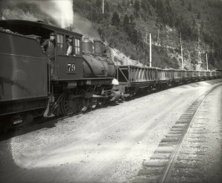 An ore train on the Northern Pacific Railroad. Two men can be seen standing in the engine car, which has the number "79" on it and is connected to the ore cars.