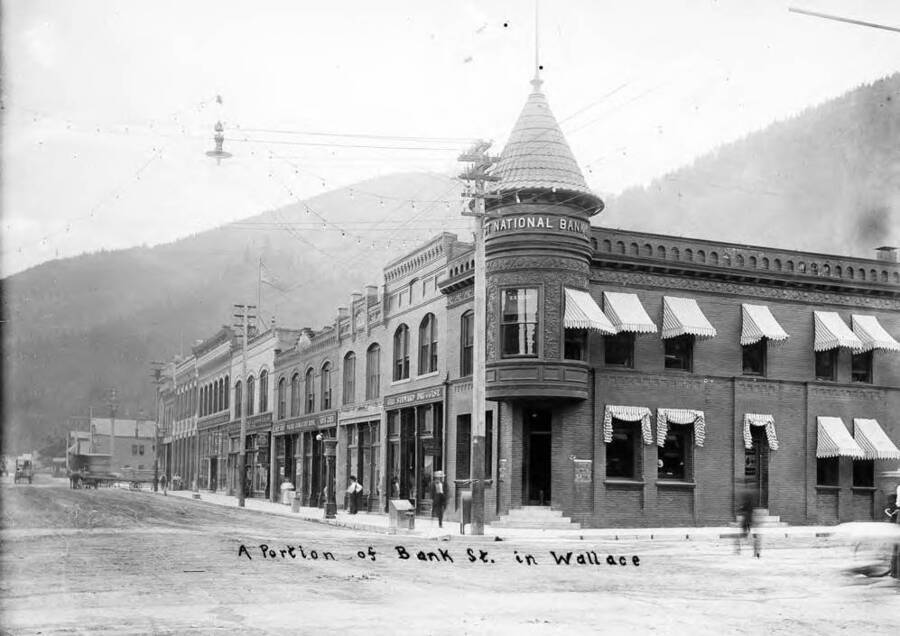 Image shows the exterior of the First National Bank and a Portion of Bank St., the south side of street between 6th and 7th in Wallace, Idaho.