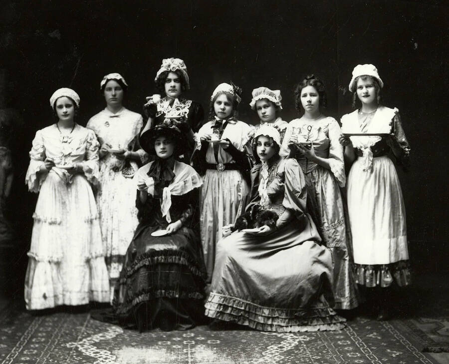 Group photos of the cast of the Wallace High School play Cranford. Nine girls are posed in costume. Five of the actresses were Marjorie Heyer, Anita McCarthy, Mildred Marshall, Mary Beale and Alice Sorenson.