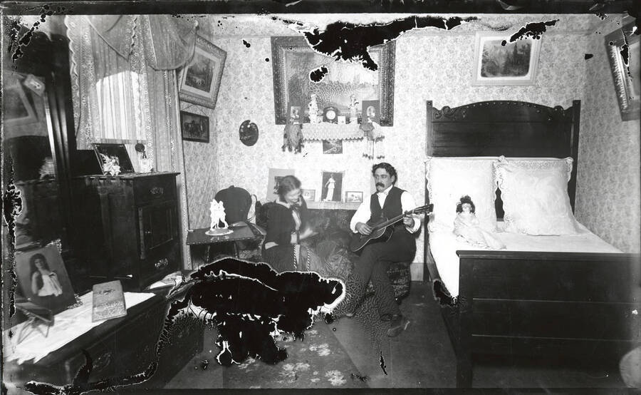 Photograph of Mr. and Mrs. Hillard. Mr. Hillard is playing guitar. The bottom left and top right corners of the negative suffered some degradation prior to being printed.