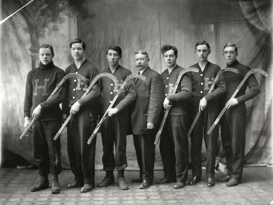 Group photo of the Hally's Roller Polo Team in Wallace, Idaho. Pictured are six males players holding sticks and the coach standing in the middle. From left to right: Will Doyle, Jack Doyle, Will Mullen, C.E. Clarke, Charles Molson, Jack Hart and Foster McLeod.
