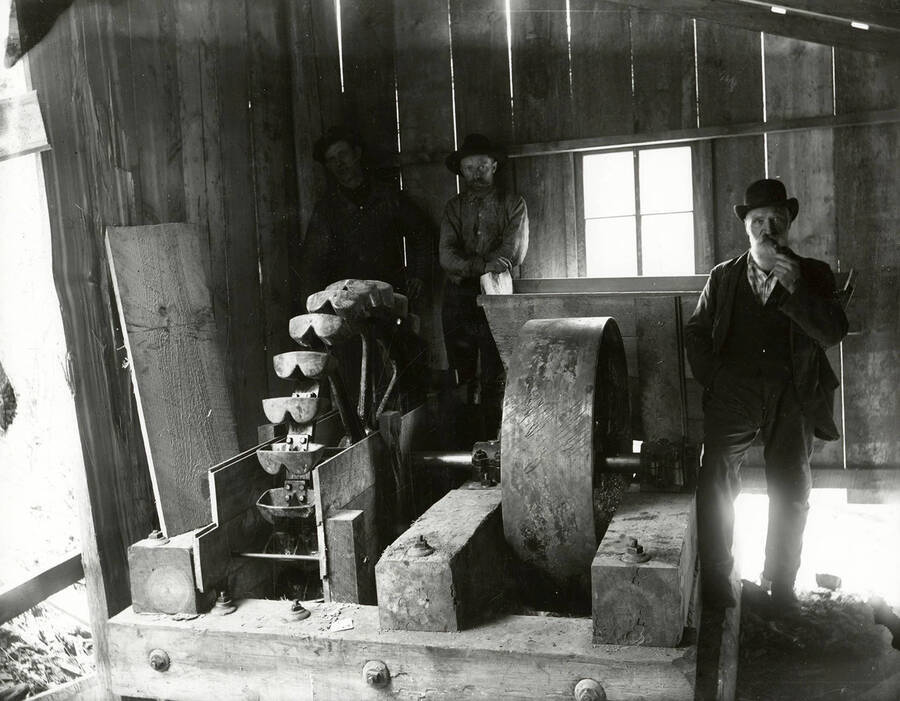 Three men standing around a Pelton wheel, an impulse-type water turbine invented by Lester Allan Pelton in the 1870s.