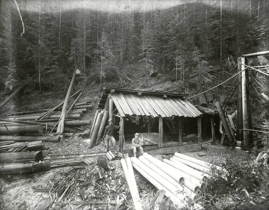 View of an unidentified mine located above Wardner, Idaho. Two men can be seen standing in front of a building on the mine.