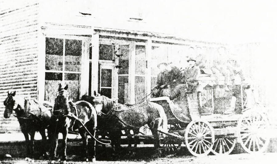 The Murray-Wallace stagecoach. Horses can be seen pulling the stagecoach as people sit in it.