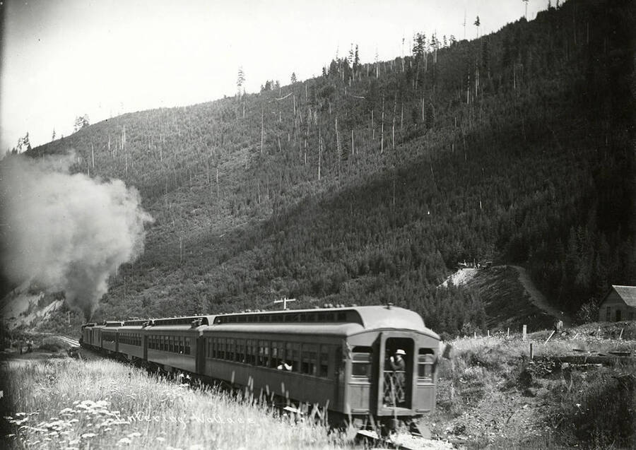A passenger train as it enters Wallace, Idaho. A man can be seen standing towards the back of the train.