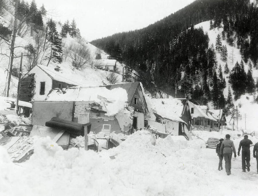 The snow slide that happened near Burke, Idaho on the Wallace side. People can be seen walking by a few houses can be seen covered in snow.