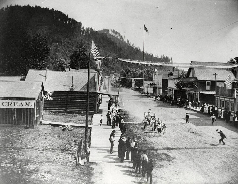 People participating in the fireman hosecart races in Murray, Idaho during Labor Day. The competition pictured is Wallace vs. Murray. Louisville Hotel can be seen on the corner.