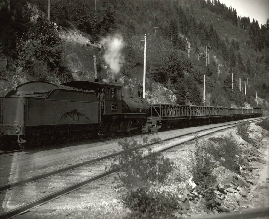 An ore train on the Northern Pacific Railroad. Two men can be seen standing in the engine car, which has the number "79" on it and is connected to the ore cars.