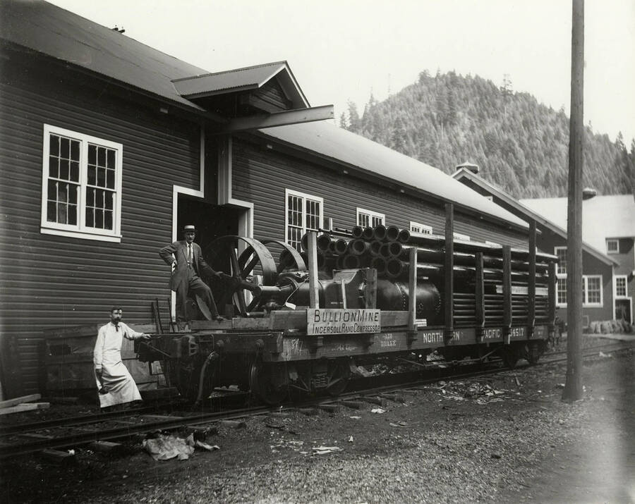 View of the Bullion Mine compressor. The compressor is loaded on a Northern Pacific flatcar beside the Coeur d'Alene Ironworks building.