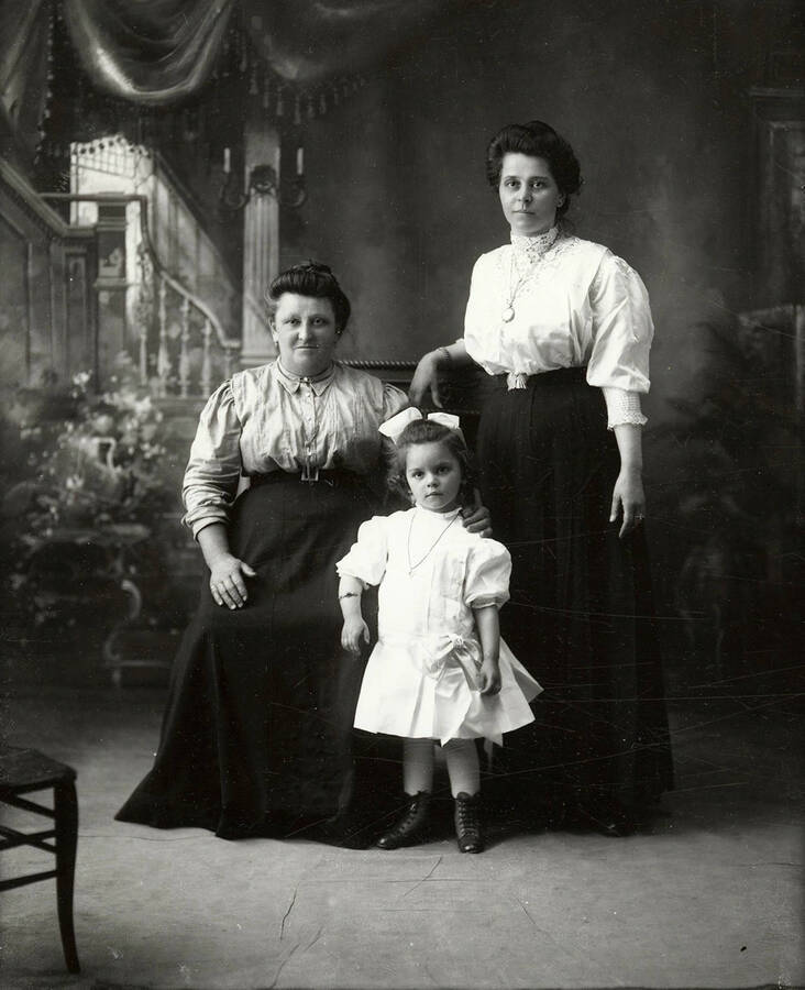 Group photo of three women. One woman is seated with a another woman and a girl, who are both standing.
