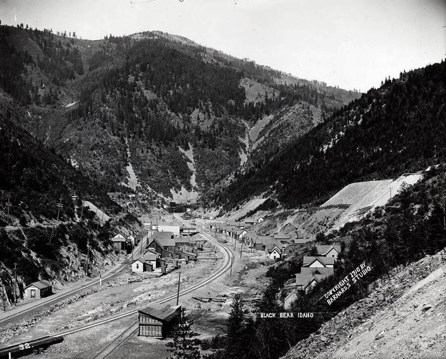 A distant view of the town Black Bear nestled in the mountains of Idaho [1910]; A railroad track is pictured going through the middle of town.