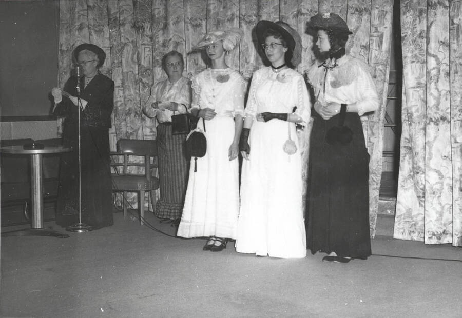 A group of ladies being announced in the fashion show at the North Idaho Press Jubilee. Two women are wearing tea dresses from the early 1900's, while one other wears a walking outfit from the later 1910's.