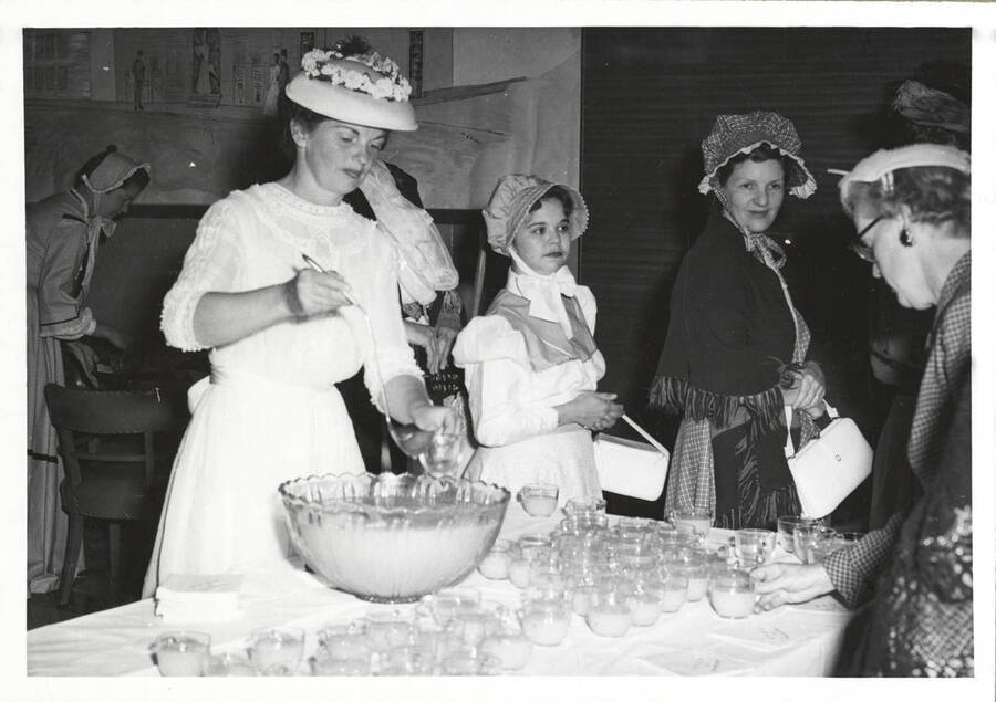 A young lady serves punch at the North Idaho Press Jubilee. Ladies are lined up in the background.