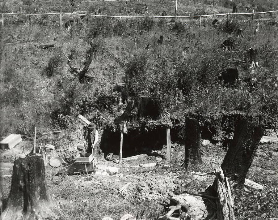 A man mining with a rocker at the Cedar Cabin place, which is located on the north side of the Coeur d'Alene Mining District.