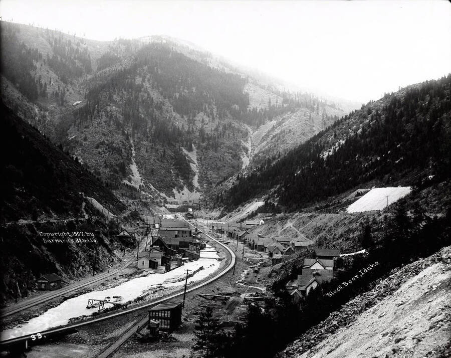 A distant view of the town Black Bear nestled in the mountains of Idaho [1907]; A railroad track is pictured going through the middle of town.