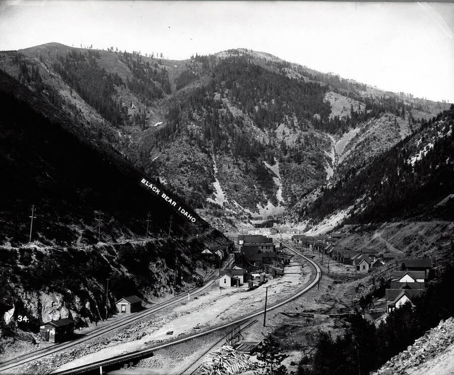 A distant view of the town Black Bear nestled in the mountains of Idaho [1906]; A railroad track is pictured going through the middle of town.