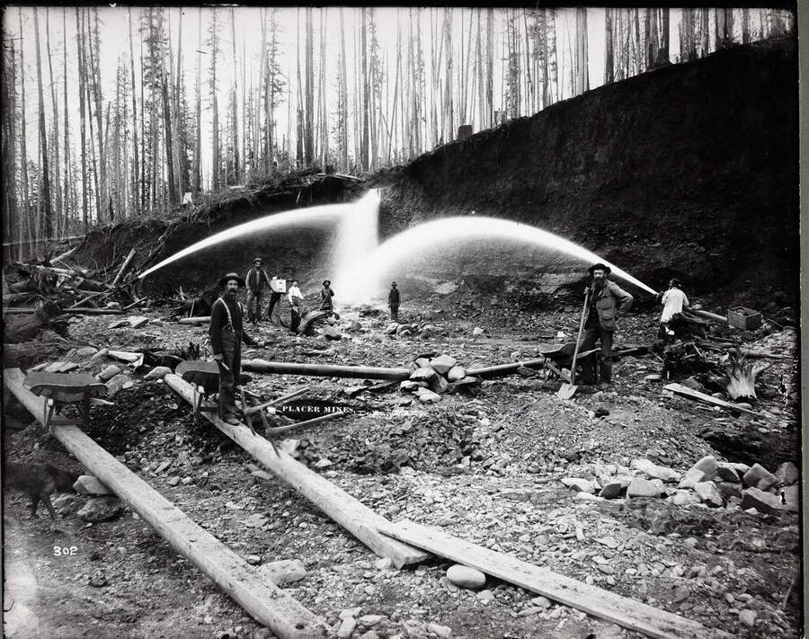 Men spraying water at mine while the miners stand around watching