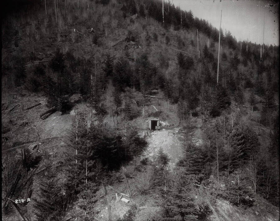Image of a wooden mine out-building. A fast-moving stream runs down the narrow gulch.