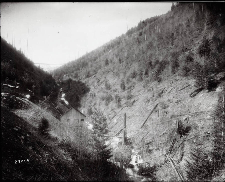 Photo of a mine portal on a hillside. An ore car sits at the mouth of the tunnel.