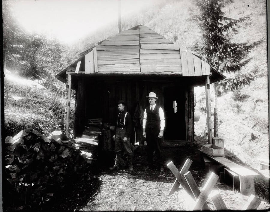 Two unidentified men standing in front of a cabin at the Standard Mine site.