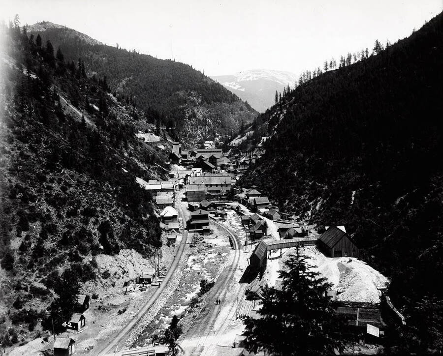 A distant view of the town of  Burke, Idaho and building of Hecla Mine; a railroad track can be seen going into town.