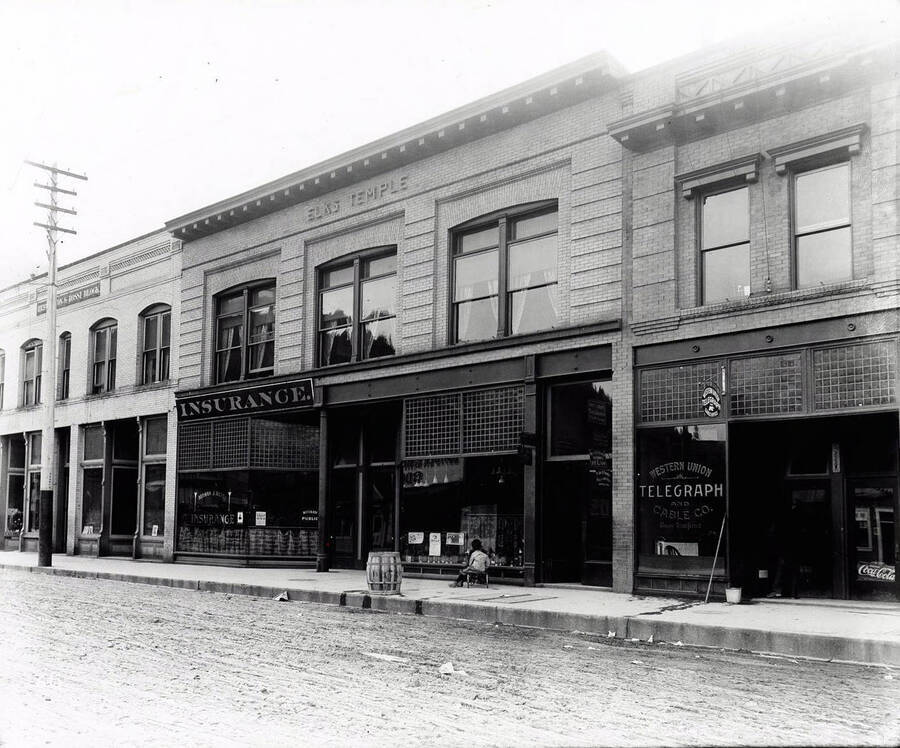 Views of the  Elks Temple, Herman J. Rossi Insurance, Western Union and other offices. An unidentified child sits in front of the Elks Temple facing the window.