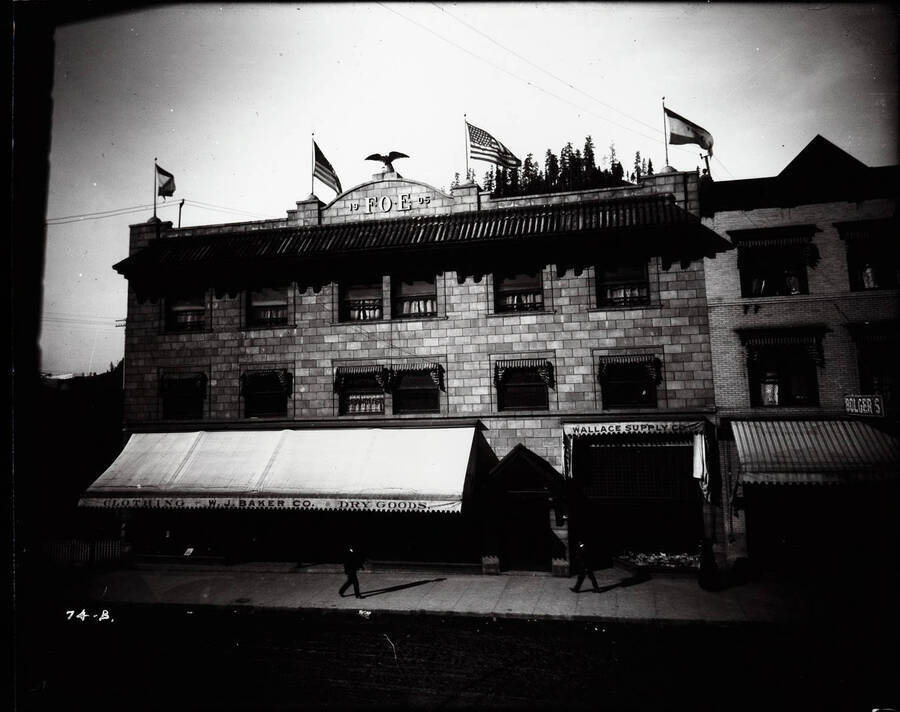 Exterior view of the Eagles block showing flags in March 1908, also shows Bolger's Wallace Supply Co., W.J. Baker Co., and other offices in Wallace, Idaho.