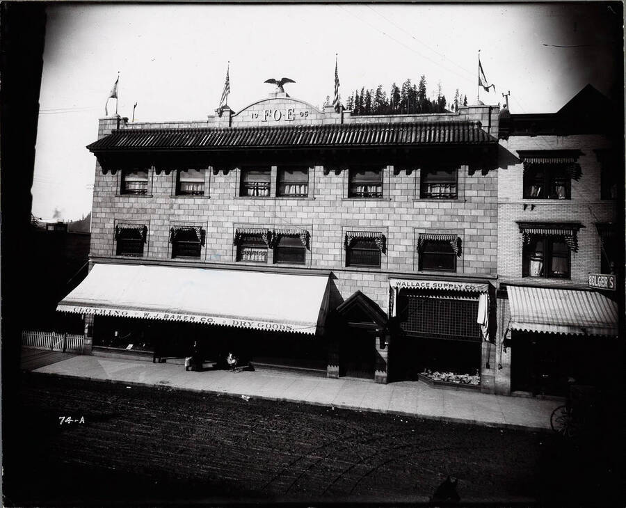 Exterior view of Eagle Block showing flags in March 1908, also shows Bolger's Wallace Supply Co., W.J. Baker Co., and other offices in Wallace Idaho.