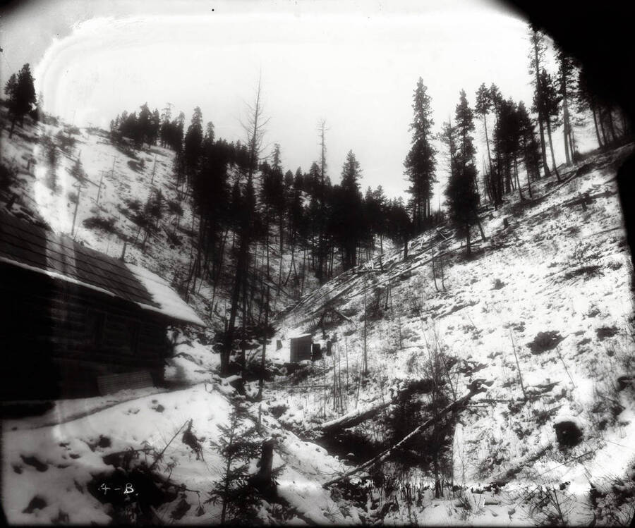A snow covered setting shows a few buildings of Beebe Bros. Mine located in a gulch.