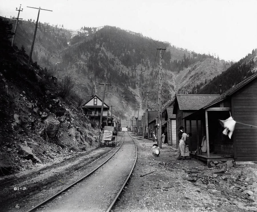 Image shows the railroad track going through the middle of town, with homes and people outside.