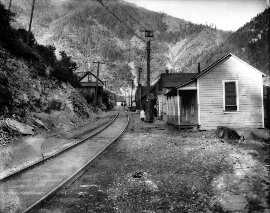 Image shows the railroad track going through the middle of town, with homes and people outside.