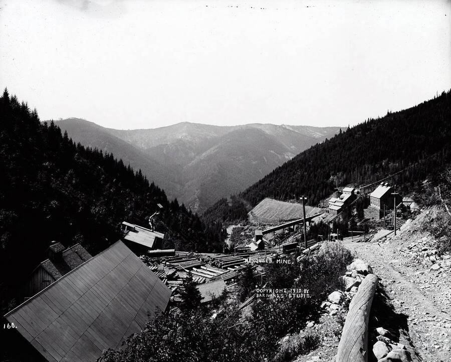 Hercules Mine in Burke, Idaho. This view, looking down on the buildings, shows the roofs of the buildings and piles of logs stacked in the yard. Caption on front: "Hercules Mine."
