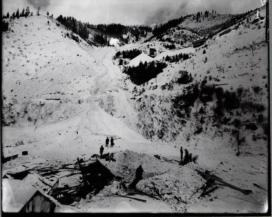 Image depicts building wreckage from a snow slide, with people standing around.