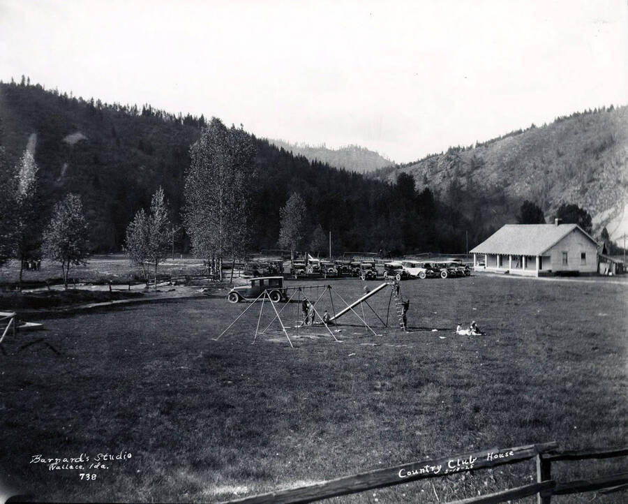 Image shows children playing on a playground in the yard of the Shoshone County Clubhouse in Kellogg, Idaho on May 18, 1925.