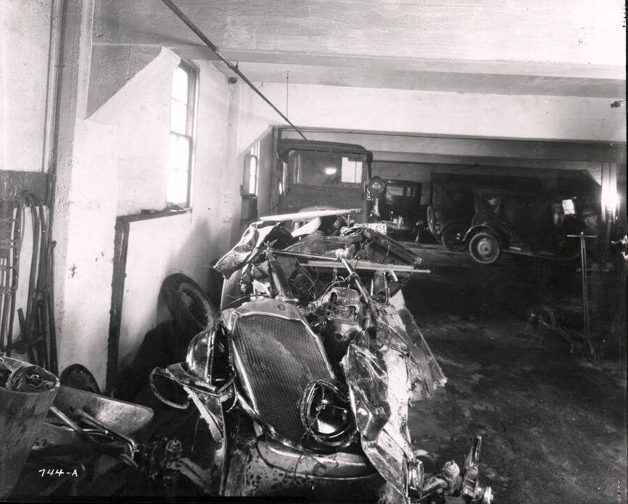 Image shows a wrecked car and other vehicles in the Wallace Garage, Wallace, Idaho, December 1925.