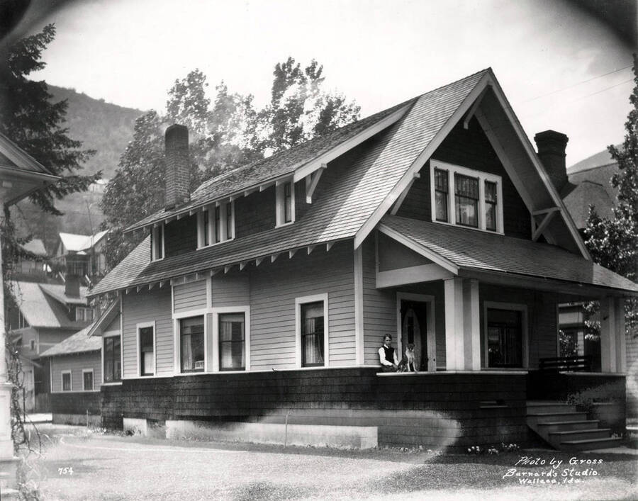 314 Cedar Street, Wallace, ID. Image shows a boy and dog sitting on the porch of Charles E. Inskip's house in Wallace, Idaho, May 1925; photo is taken by Gross for Barnard's Studio. Charles E. Inskip was the partner of "Inskip & English Plumbing & Heating Co." in Wallace.