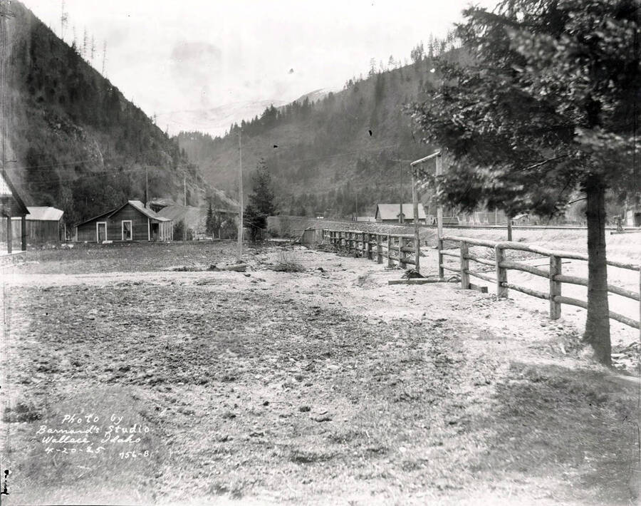 Image shows a railroad track, wood fence and open yard of the Lee property in Wallace, Idaho, April 20, 1925.