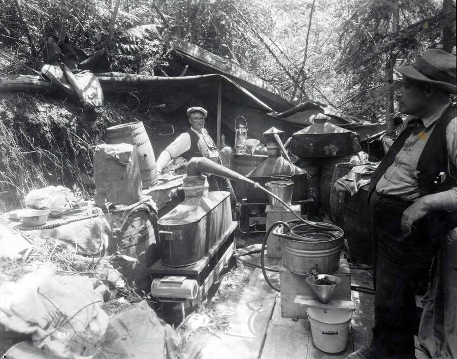 Image shows a Still near Silver Cliff Mine above Pottsville, Idaho. Charlie Bloom is on the left and Sheriff Rene Edward Weniger is on the right.