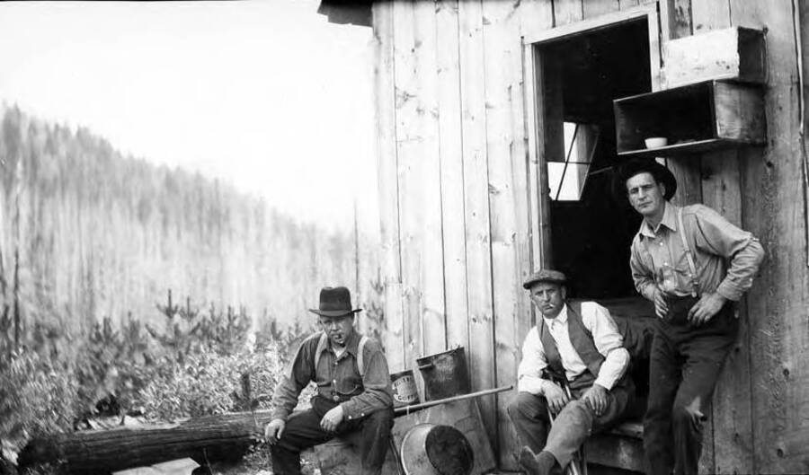 Group of men sitting out side one of them is smoking a pipe