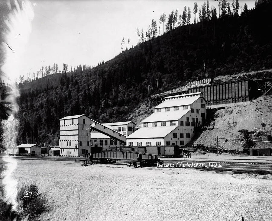 Image of the Hercules Concentrating Mill and its associated buildings in Wallace, Idaho. Railroad tracks run in front.