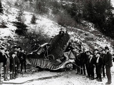 Photo shows metal debris from a Northern Pacific Railroad engine explosion. A large group of men and children pose along each side.