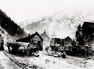 Close-up view of the Northern Pacific train engine explosion debris. Various citizens can be seen examining the wreckage, which has come close to some of the houses.