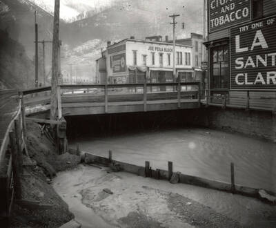 Gilmore's (cigars and tobacco) on the bank of the Coeur d'Alene River, right next to the bridge, in Wallace, Idaho. Taken for H.L. Day.