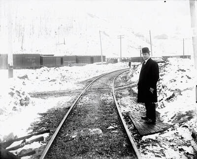 Close-up of a man standing next to some Oregon, Washington Railroad & Navigation Company tracks. Caption on front: "O.W.R. and N. Accident Case, 1913 Edge of Wallace."