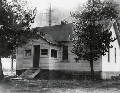 View of a house in Wallace, Idaho with trees in front of it and a hill in the background. A real estate view taken for Idaho First National Bank.