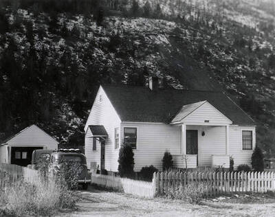 View of a house in Wallace, Idaho with a fence around it and cars parked in the driveway. A real estate view taken for Idaho First National Bank.