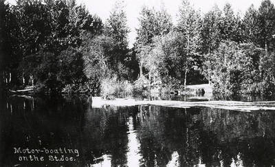 View of St. Joe River, with trees along the bank and people motorboating on the river.