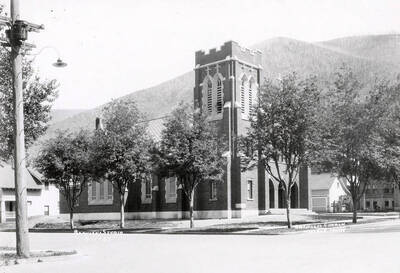 Exterior view of St. Alphonsus Catholic Church in Wallace, Idaho. The church sits on a street corner and has trees planted out front.