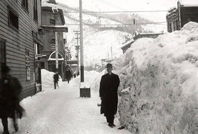 Looking down Cedar Street during the winter in Wallace, Idaho. Residents are walking next to buildings in the snow.